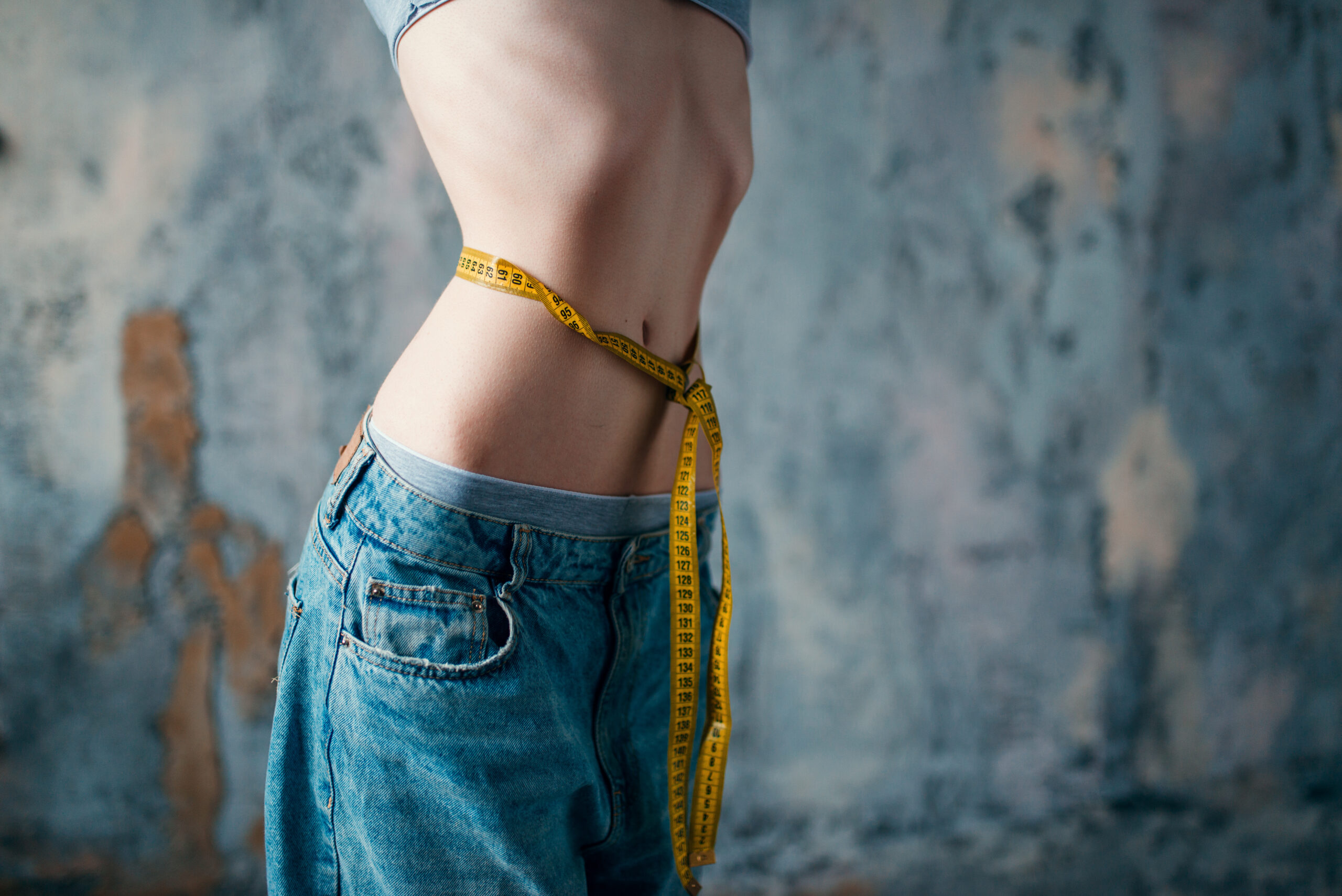 Thin woman in jeans measures her waist, weight loss, anorexia. Fat or calories burning concept, medical illness
