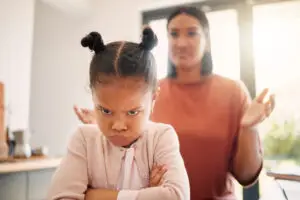angry child with arms crossed while parent behind wonders why child is more aggressive on leuvocorin
