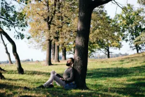 young man sitting against tree in las vegas feeling depressed despite summer sun needing to go to mindwell psychiatric services