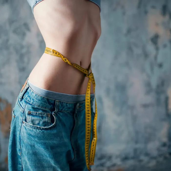 Thin woman in jeans measures her waist, weight loss, anorexia. Fat or calories burning concept, medical illness