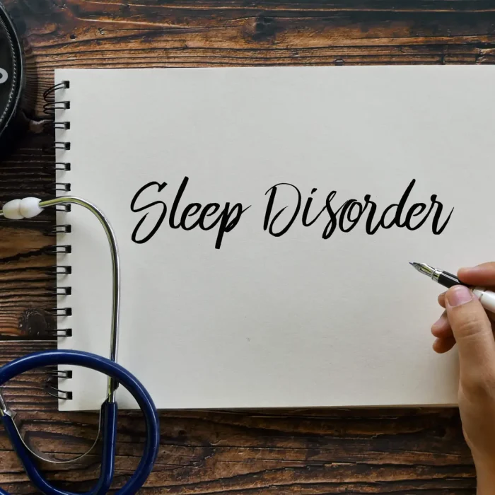 Top view of clock, stethoscope, and hand holding pen writing Sleep Disorder on notebook on wooden background.