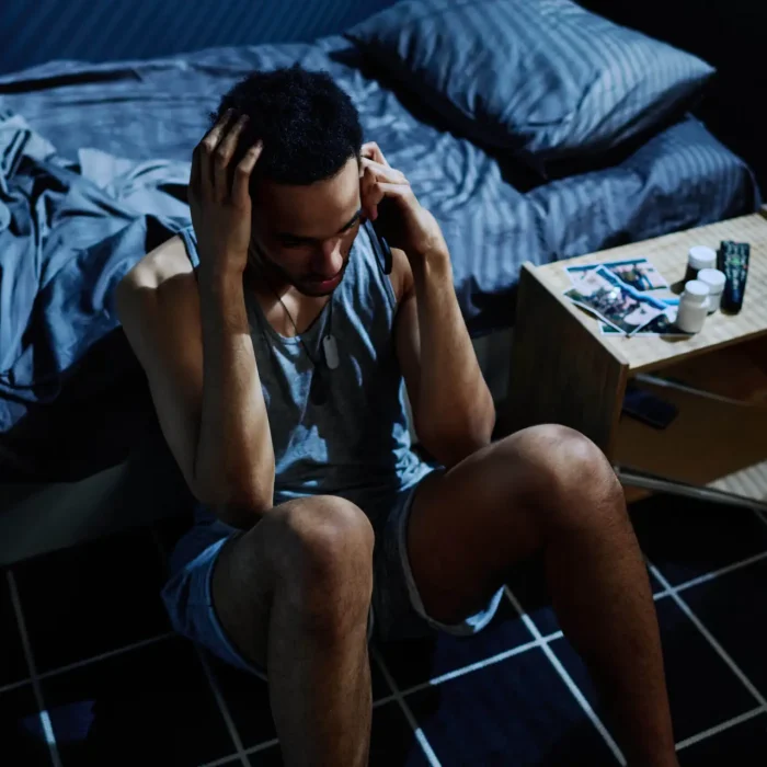 Guy with post traumatic syndrome calling 911 to get psychological help or consultation of specialist while sitting by bed on the floor